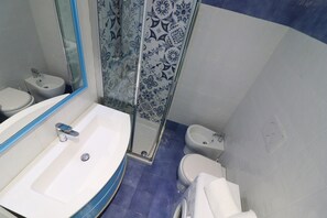 Une salle de bain avec un lavabo blanc, un bidet, des toilettes et une douche dotée d’une porte en verre.