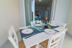 A dining table set for two with white chairs, a blue tablecloth, and a bottle of wine.