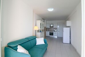 A compact living space with a teal sofa, a kitchen area with white cabinets, and a refrigerator.