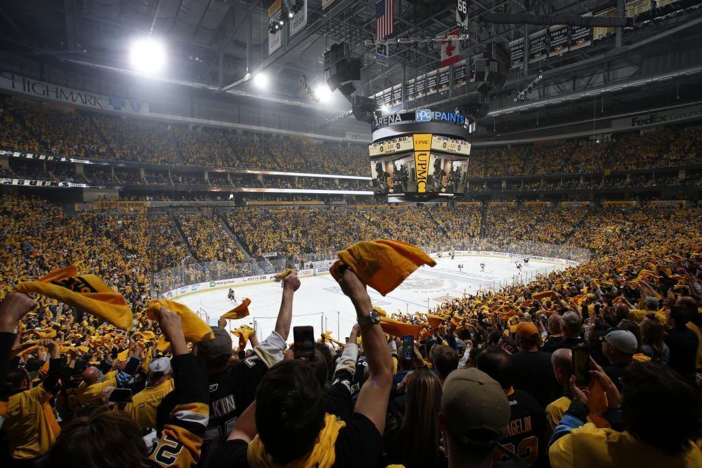 A large indoor stadium with multiple levels of seating, a central ice rink, and a scoreboard.