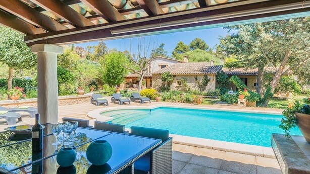 A poolside area with lounge chairs, a table with a bottle and glasses, and a view of a house with a tiled roof. - Beautiful Villa Papalaia with Pool, Garden, Terraces, Air Conditioning (Pollensa)