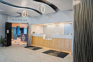 A reception area with a modern design, including a reception desk, a waiting area with seating, and a patterned wall. - Balcony Coffee, Beach All Day (Virginia Beach)