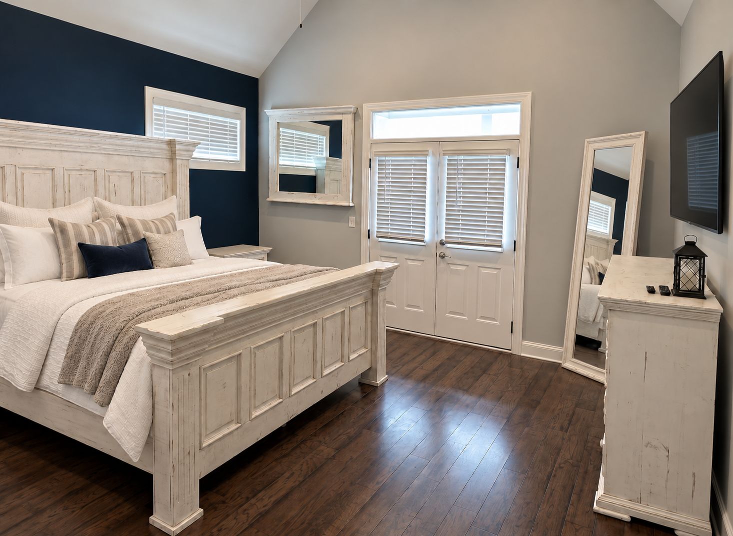 A bedroom with a large bed, a dresser, a mirror, and a television.