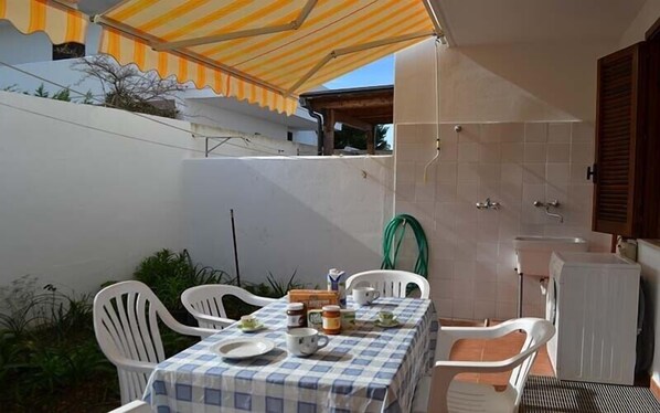 A patio with a table set for two, a green hose, and a white cabinet. - Charming Holiday Apartment "Casa a Torre dell'Orso PT55" with Garden (Torre dell'Orso)