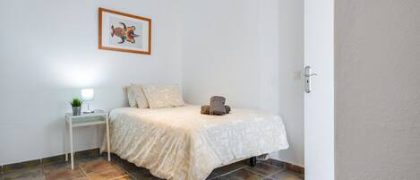 A bedroom with a bed, a bedside table with a lamp, a framed picture on the wall, and a door.