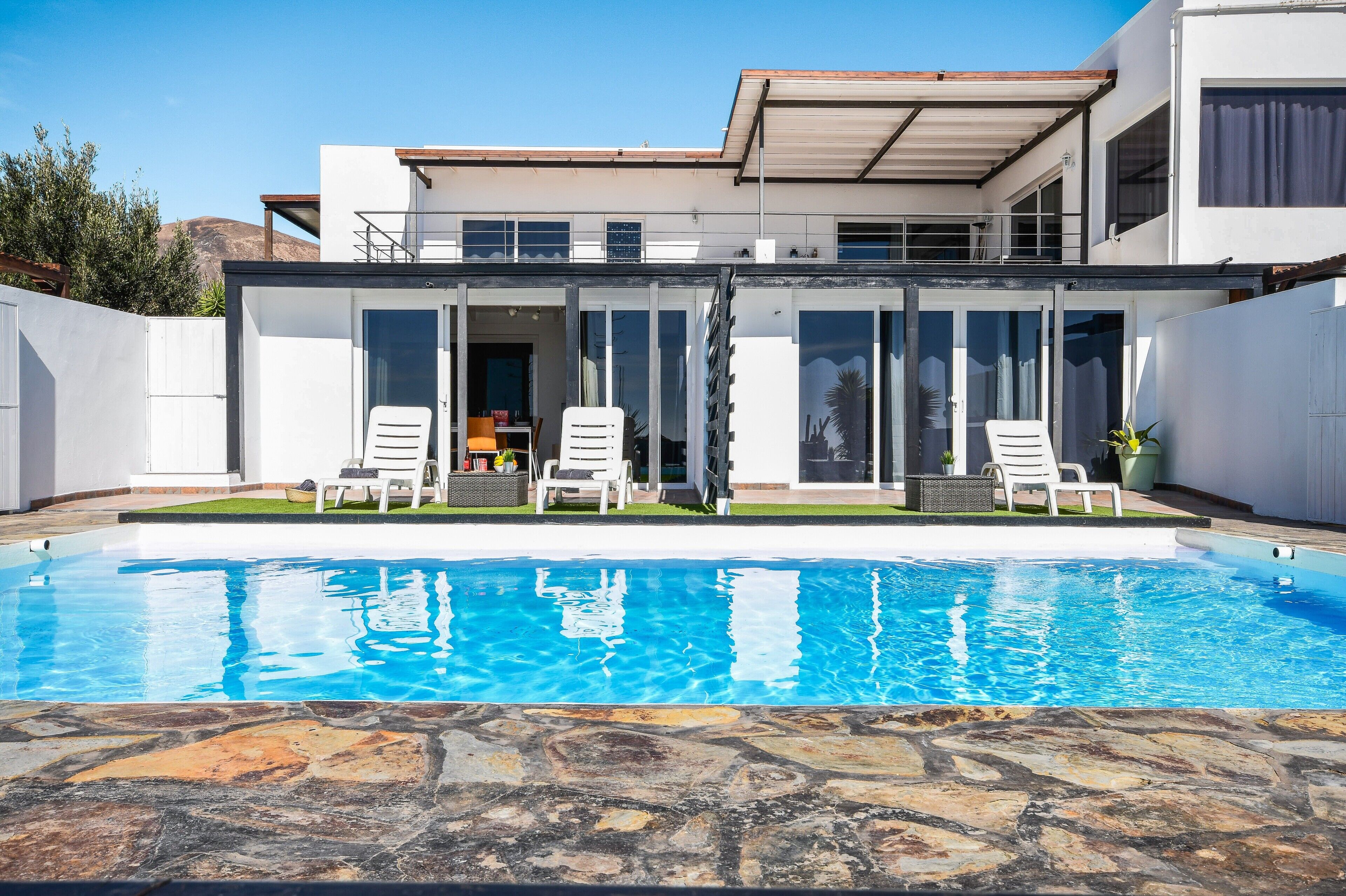A modern house with a swimming pool, glass doors, and outdoor seating.