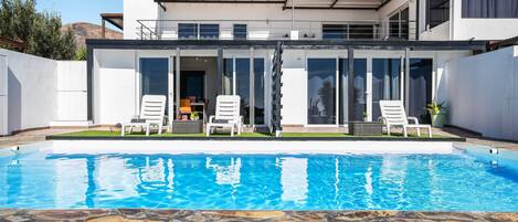 A modern house with a swimming pool, glass doors, and outdoor seating.
