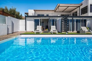 Une maison moderne dotée d’une piscine, de deux chaises longues et d’un patio couvert.