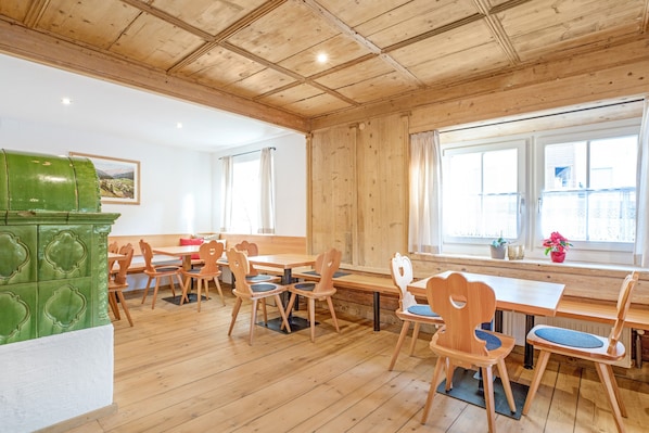 A restaurant with wooden tables and chairs, a green stove, and large windows.