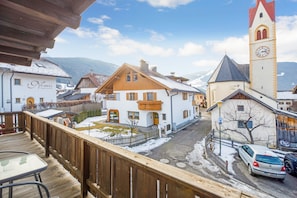 A wooden deck overlooking a town with a clock tower, a white building labeled 'Nomi's Apartments,' and a parked car.