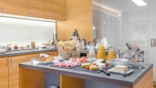 A modern kitchen with wooden cabinets, a marble countertop, and various food items.