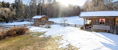 A wooden cabin with a snow-covered roof, a wooden fence, and a clear view of the surrounding forest and mountains.