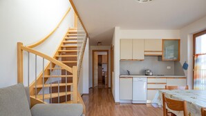 Una escalera conduce a un dormitorio tipo loft, una cocina con armarios blancos y un comedor con mesa y sillas.