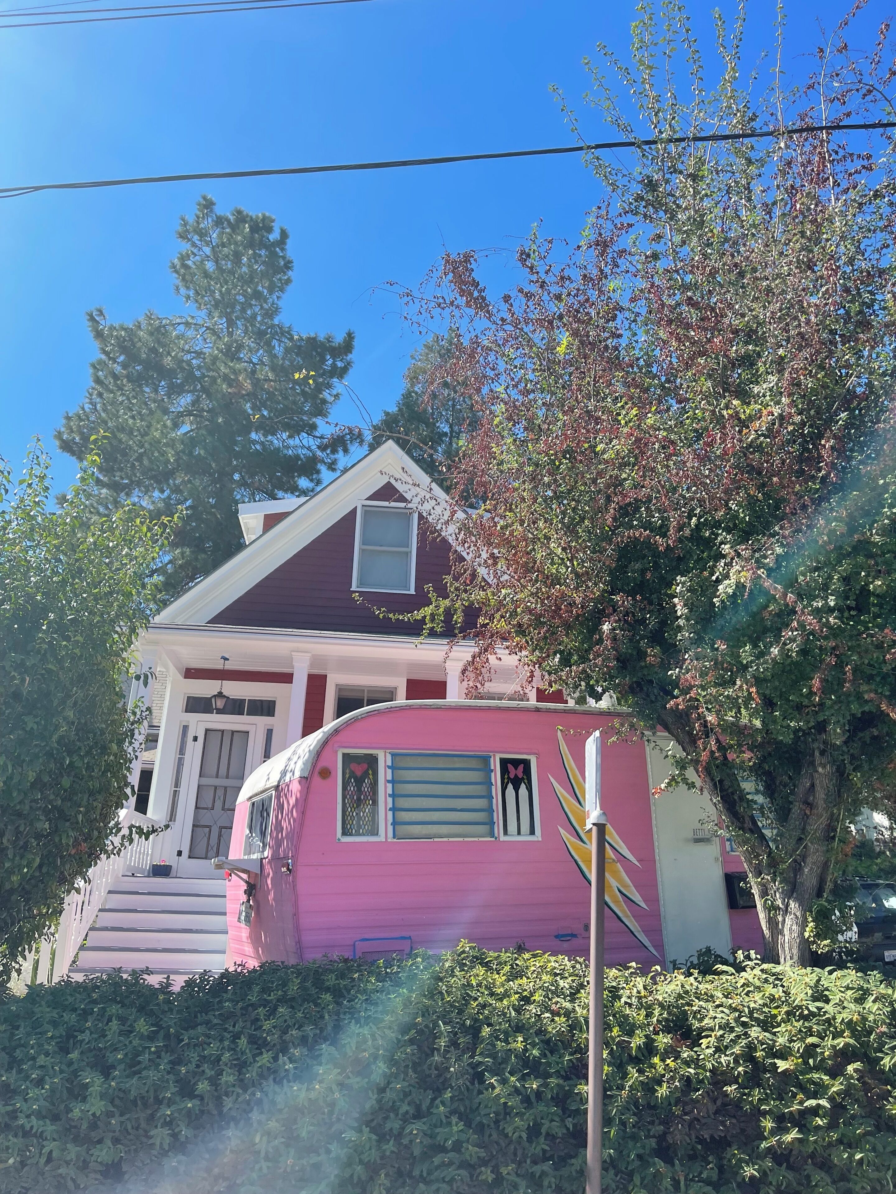 A house with a pink trailer attached, surrounded by greenery and a clear blue sky.