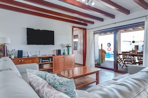 A modern living room with a flat-screen TV, wooden furniture, and a sliding glass door leading to an outdoor area.