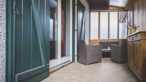 Un patio techado con mobiliario de mimbre, un armario de madera y vistas a través de amplios ventanales.