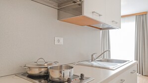 Una cocina moderna con estufa integrada, dos ollas, un lavamanos y una ventana con cortinas.
