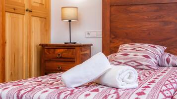 Una cama bien hecha con una colcha estampada, una mesita de noche de madera con una lámpara y un armario de madera.