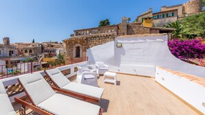 Eine Dachterrasse mit Liegestühlen, einem kleinen Tisch und Blick auf die umliegenden Gebäude.