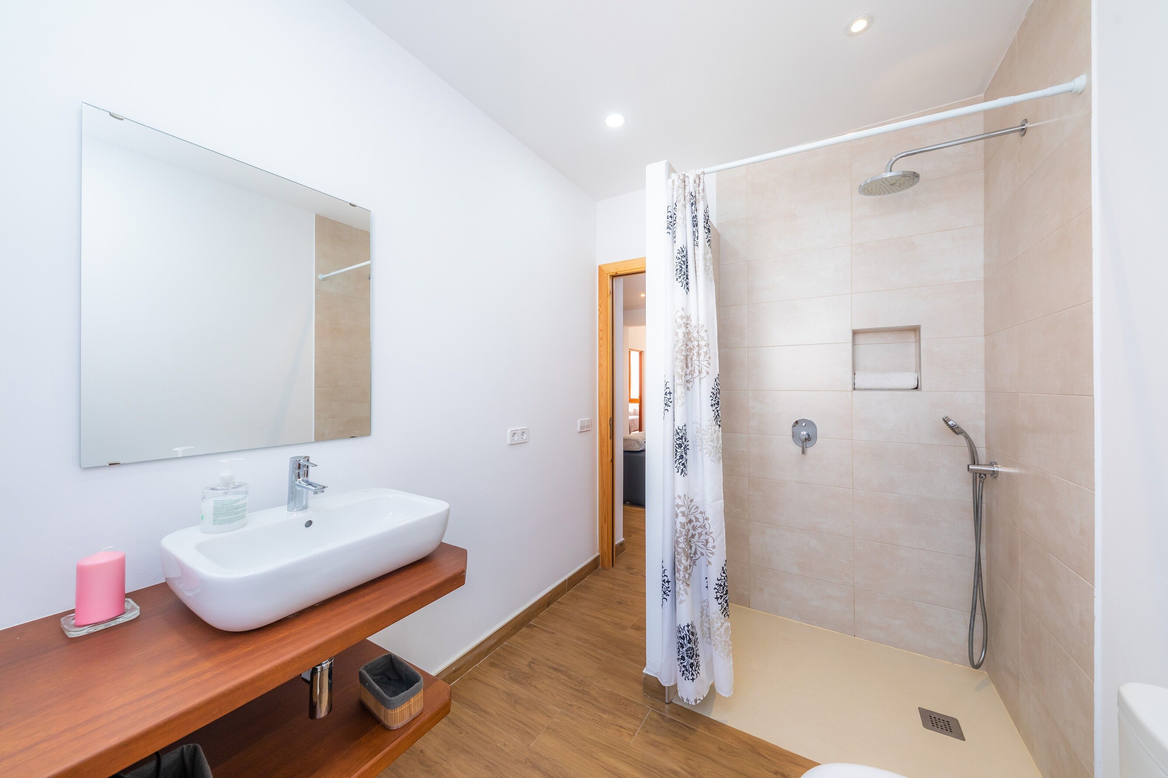 A bathroom with a white sink, mirror, shower, and wooden vanity.