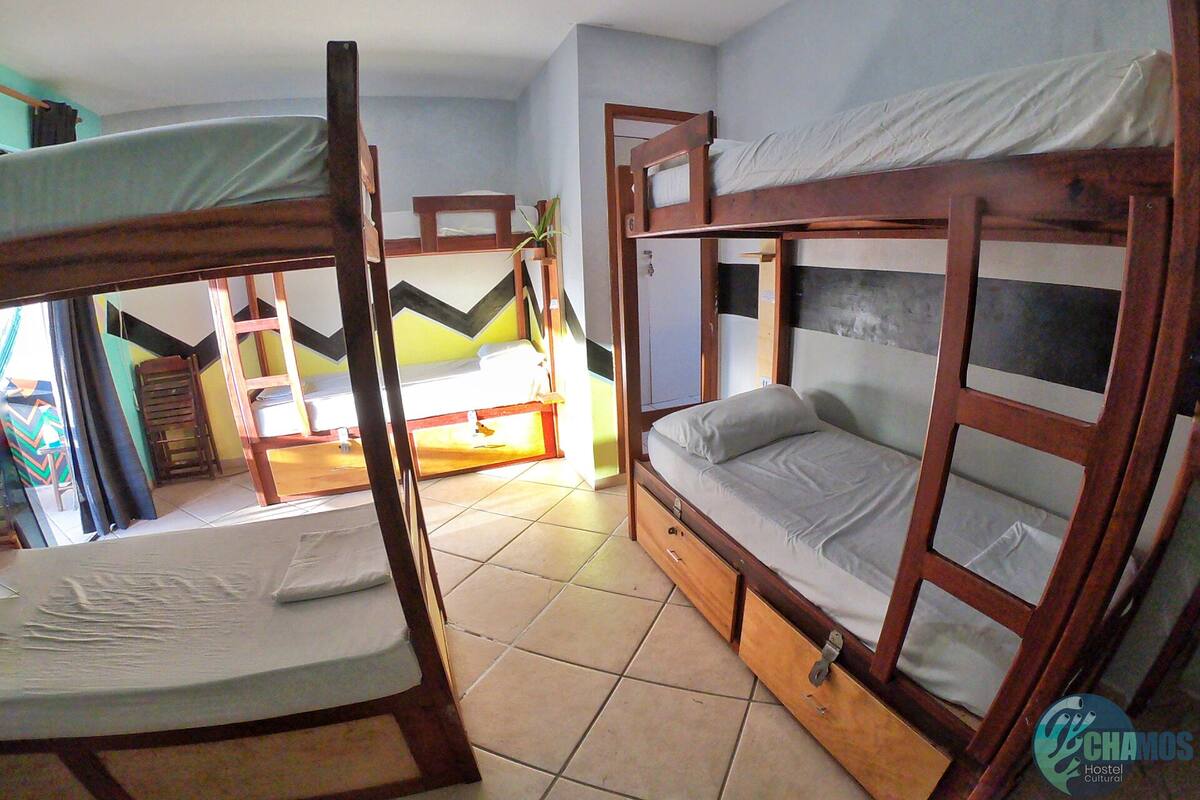 A dormitory room with bunk beds, a wooden wardrobe, and a tiled floor.