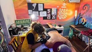 Un estudio de tatuajes con un mural colorido, un abanico y diversos diseños de tatuajes en la pared.