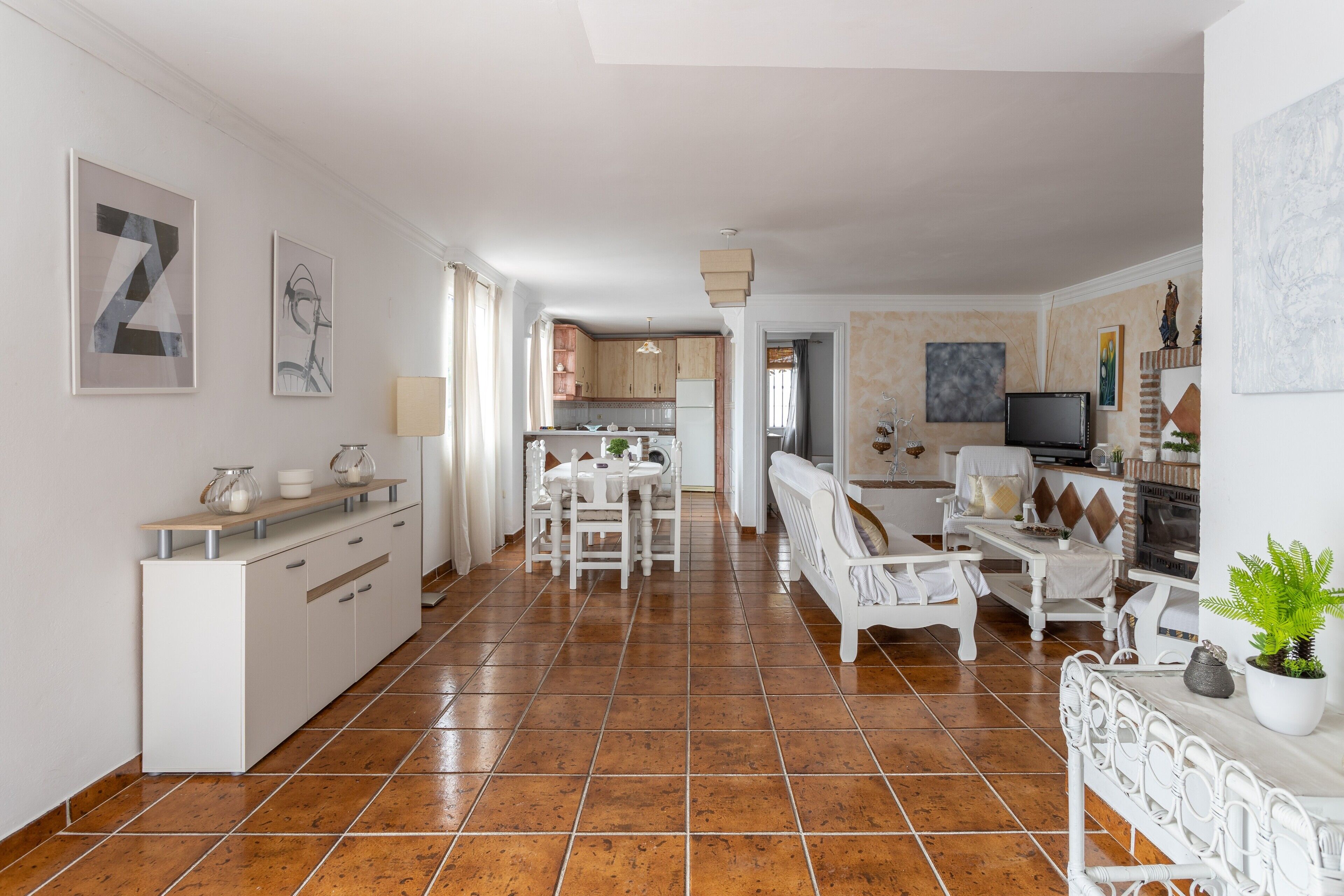 Ein geräumiges Wohnzimmer mit Esstisch, weißen Möbeln und einer Küche im Hintergrund.
