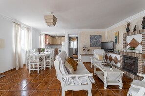 A spacious living room with a fireplace, a dining area, and a kitchen in the background.
