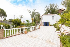 A white building with a blue door, surrounded by a white fence and potted plants.