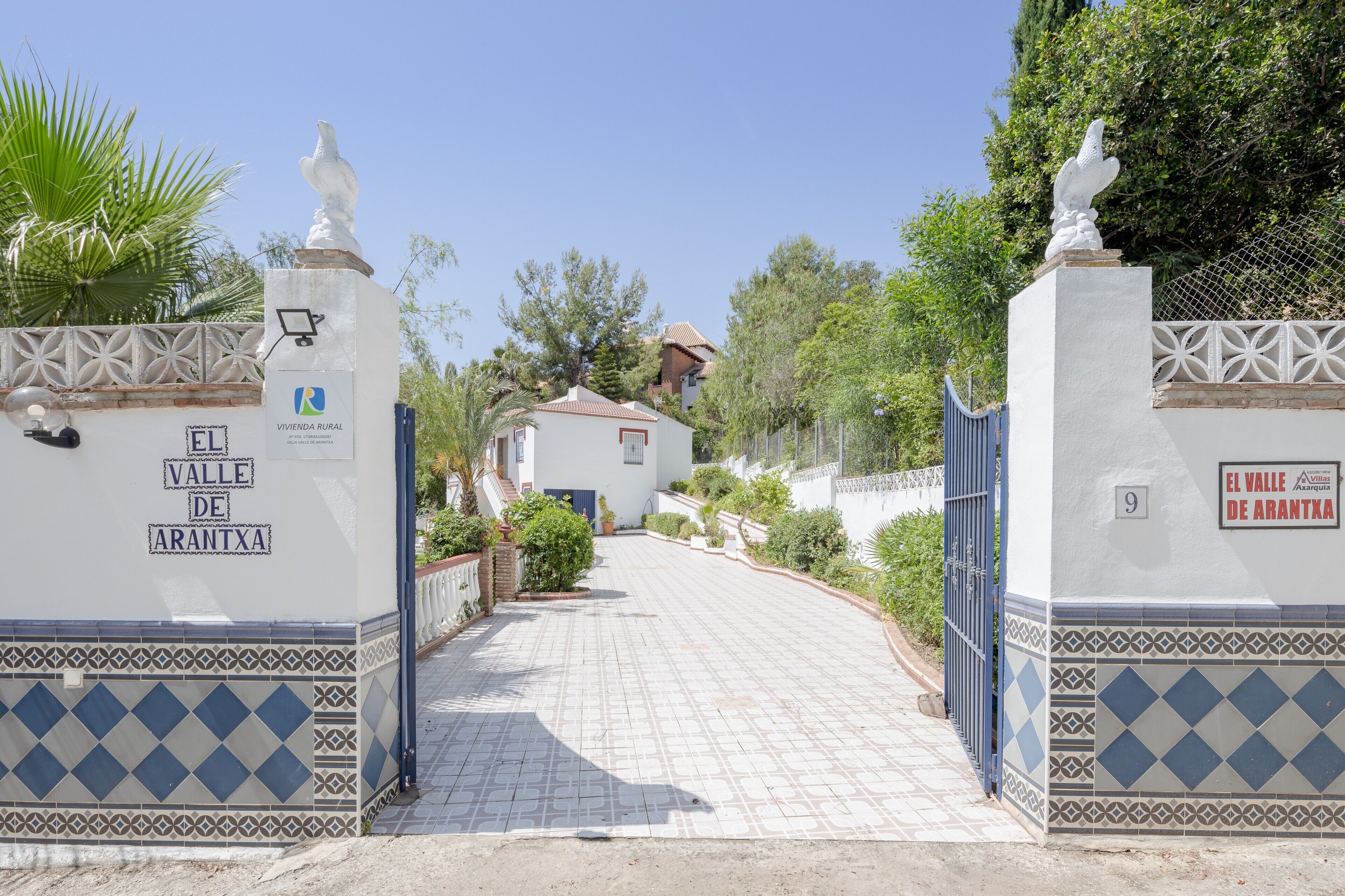 A gated entrance with a tiled pathway leading to a building, surrounded by greenery.
