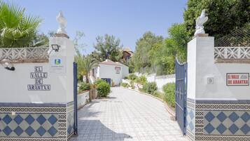 A gated entrance with a tiled pathway leading to a building, surrounded by greenery.