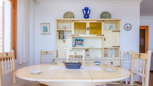 A dining area with a round table, four chairs, a blue basket, and a white cabinet with glass doors. -  Central Apartment at the Beach Promenade with Wi-Fi and Sea View (Cala Millor)