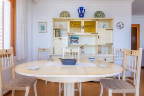 Un comedor con una mesa redonda, cuatro sillas, una cesta azul y un armario blanco con puertas de cristal.