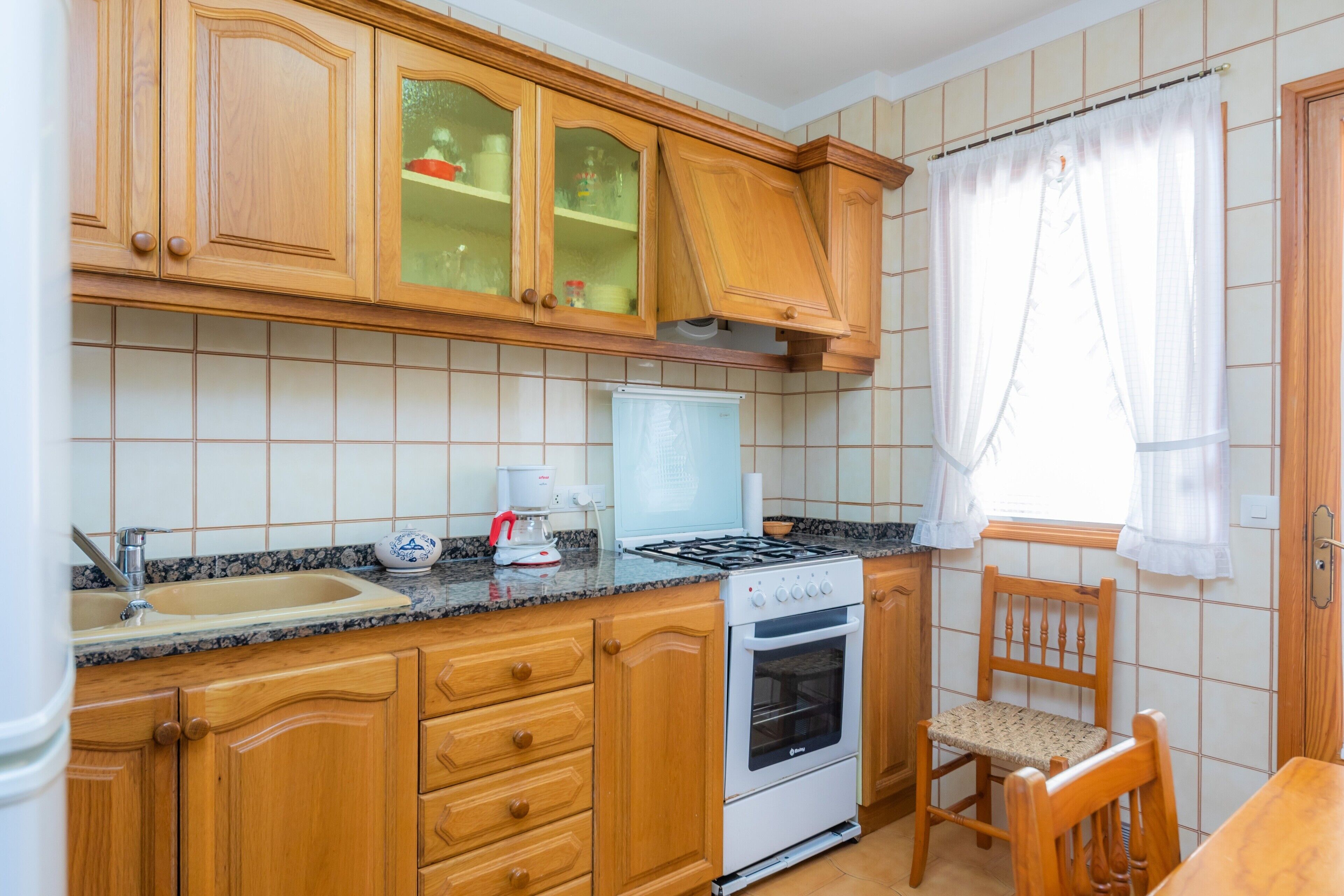A kitchen with wooden cabinets, a stove, a sink, and a chair.