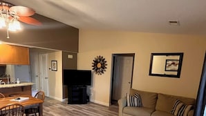 A living room with a wooden floor, a sofa, a coffee table, a TV, and a ceiling fan. - Gated / Indoor and Outdoor pools Overlooking hole 17 Pointe Royale Golf Course (Branson)