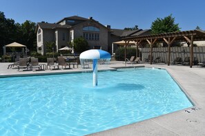 A swimming pool with a water fountain, lounge chairs, and a covered seating area.