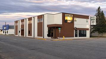 A two-story building with a sign for River Inn, featuring a flat facade with a mix of brown and white panels, a visible entrance, and a fire hydrant on the sidewalk.