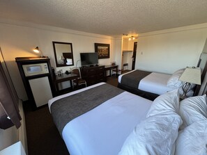 Une chambre d’hôtel avec deux lits, un bureau avec un ordinateur, une télévision et un four à micro-ondes.