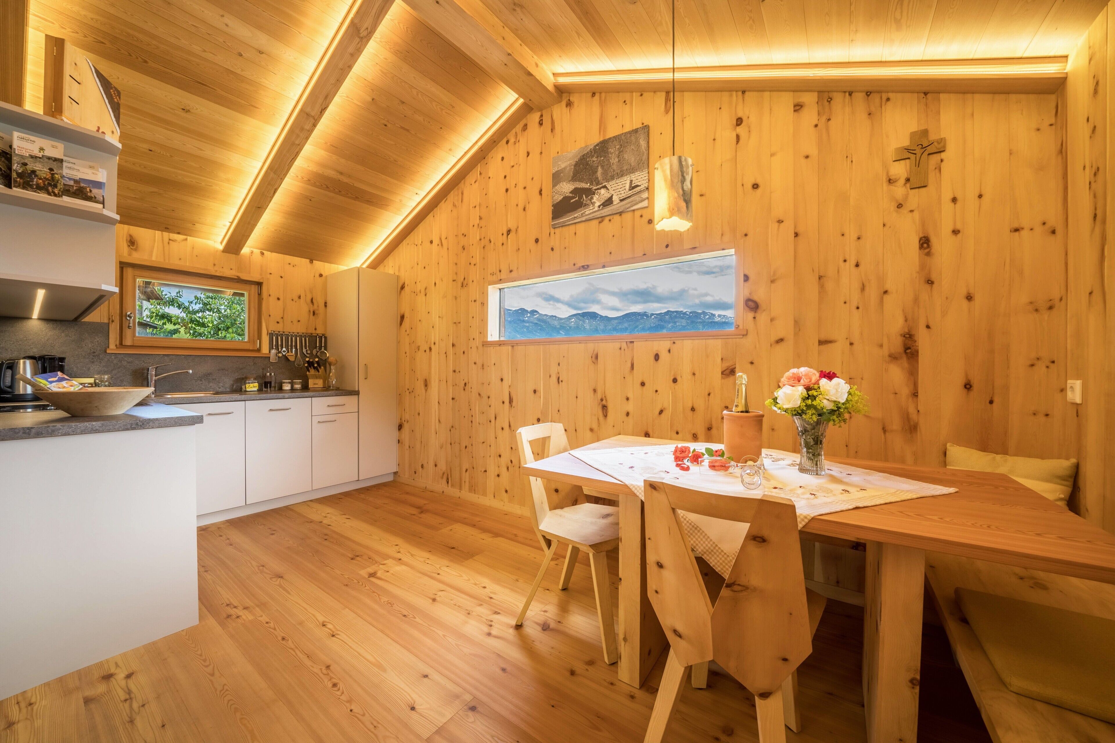 A wooden interior with a dining table, chairs, a kitchen area, and a window with a mountain view.