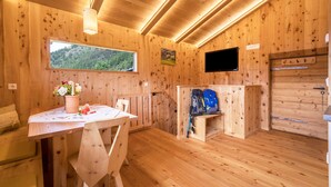 A wooden cabin interior with a dining table, chairs, a window with a view, a television, and a door.