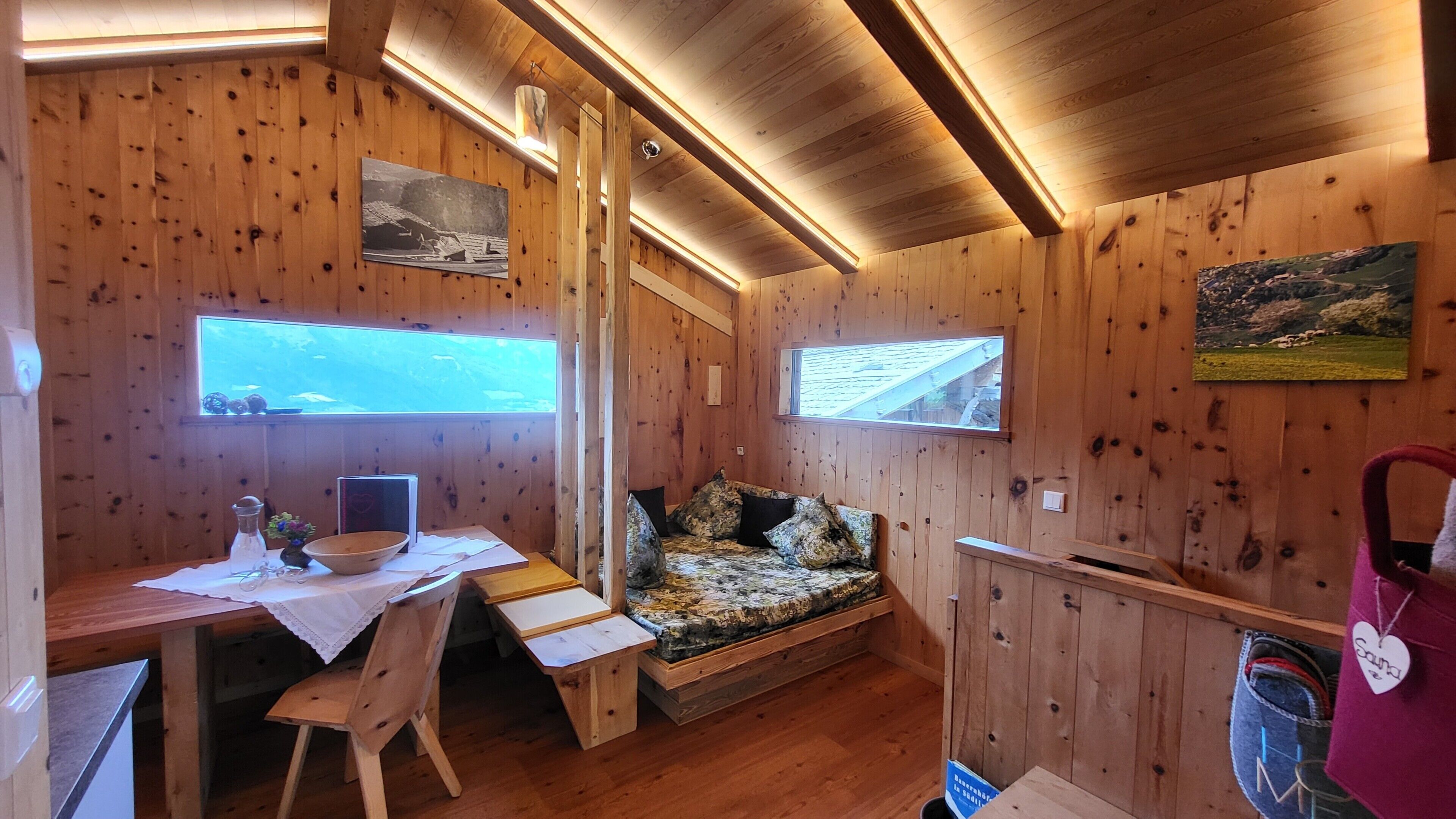 Eine Holzhütte mit Schreibtisch und Stuhl, einem Bett mit gemusterten Betttextilien und zwei Fenstern.