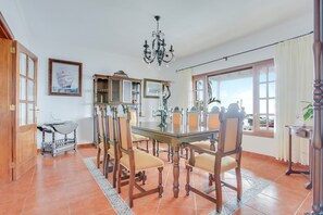 Un comedor con una mesa grande, sillas, una lámpara de araña y vistas al exterior.