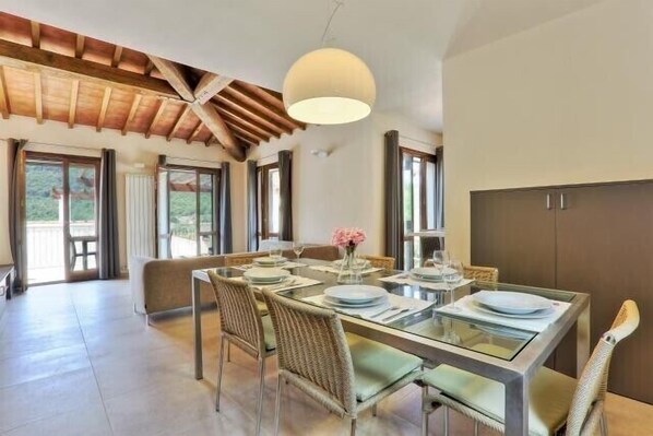 Un coin repas avec une table en verre, des chaises en osier, un luminaire suspendu et une vue sur l’extérieur.