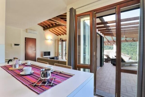 A modern kitchen with a dining area, large windows, and a view of the outdoors.