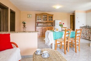 Ein Zimmer mit Esstisch, Stühlen, Küchenzeile und einem Bett mit rotem Kissen.