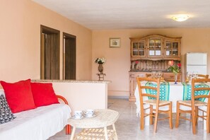 Ein Wohnzimmer mit einer Couch, einem Esstisch mit Stühlen, einer Küchenzeile und einem Kühlschrank.