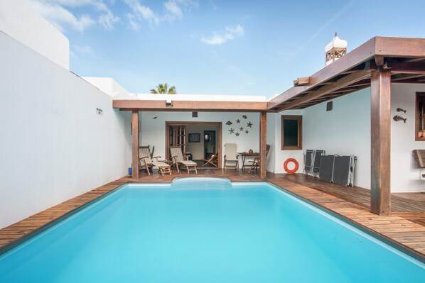 A swimming pool with wooden deck, lounge chairs, and a covered patio area.
