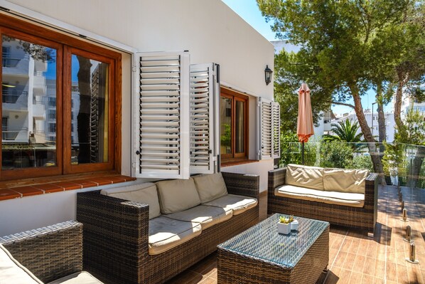 A balcony with wicker furniture, a glass table, and a view of the surrounding buildings.