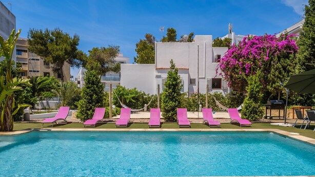 A swimming pool with pink lounge chairs, surrounded by greenery and modern buildings.