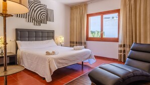 A hotel room with a bed, a chair, a lamp, and a window with curtains.